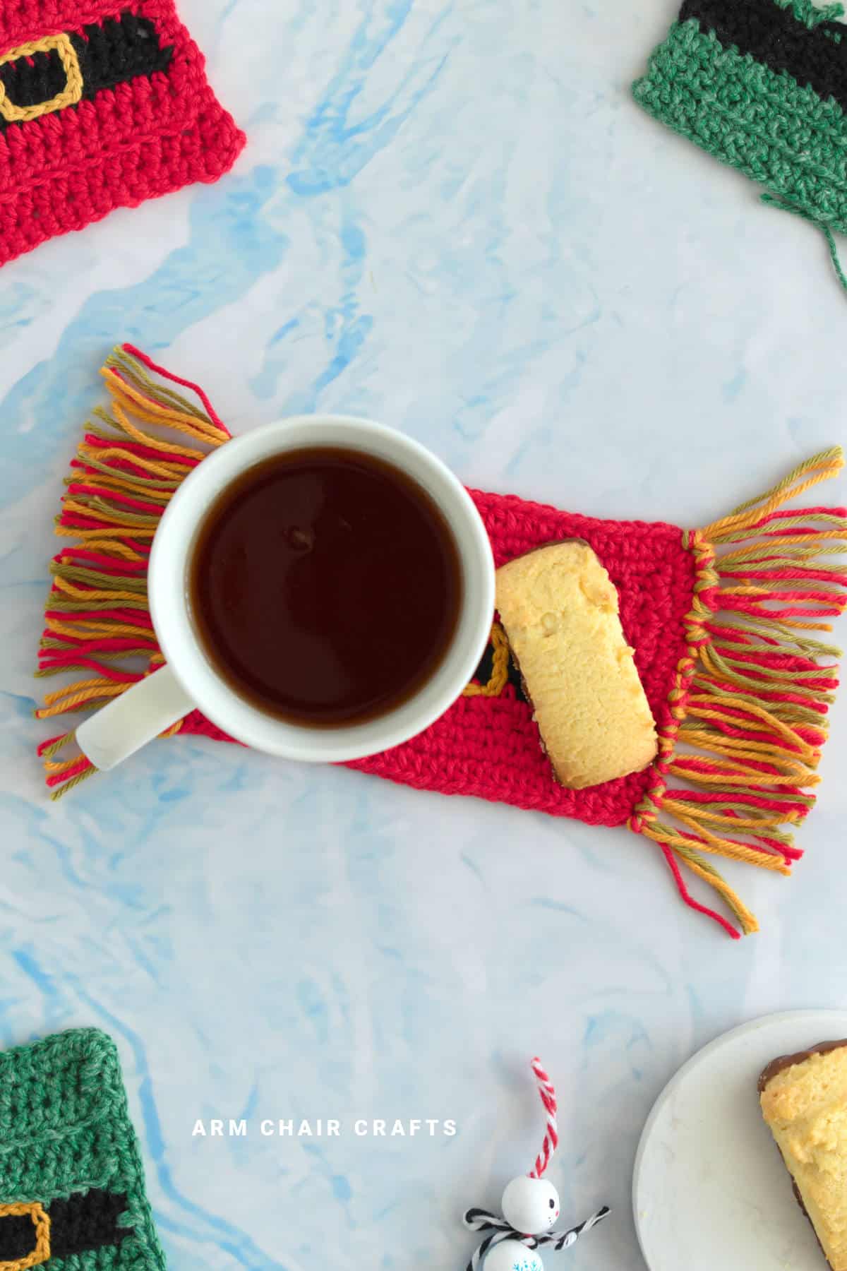Crochet mug rug with a cup of tea and biscuit on top.
